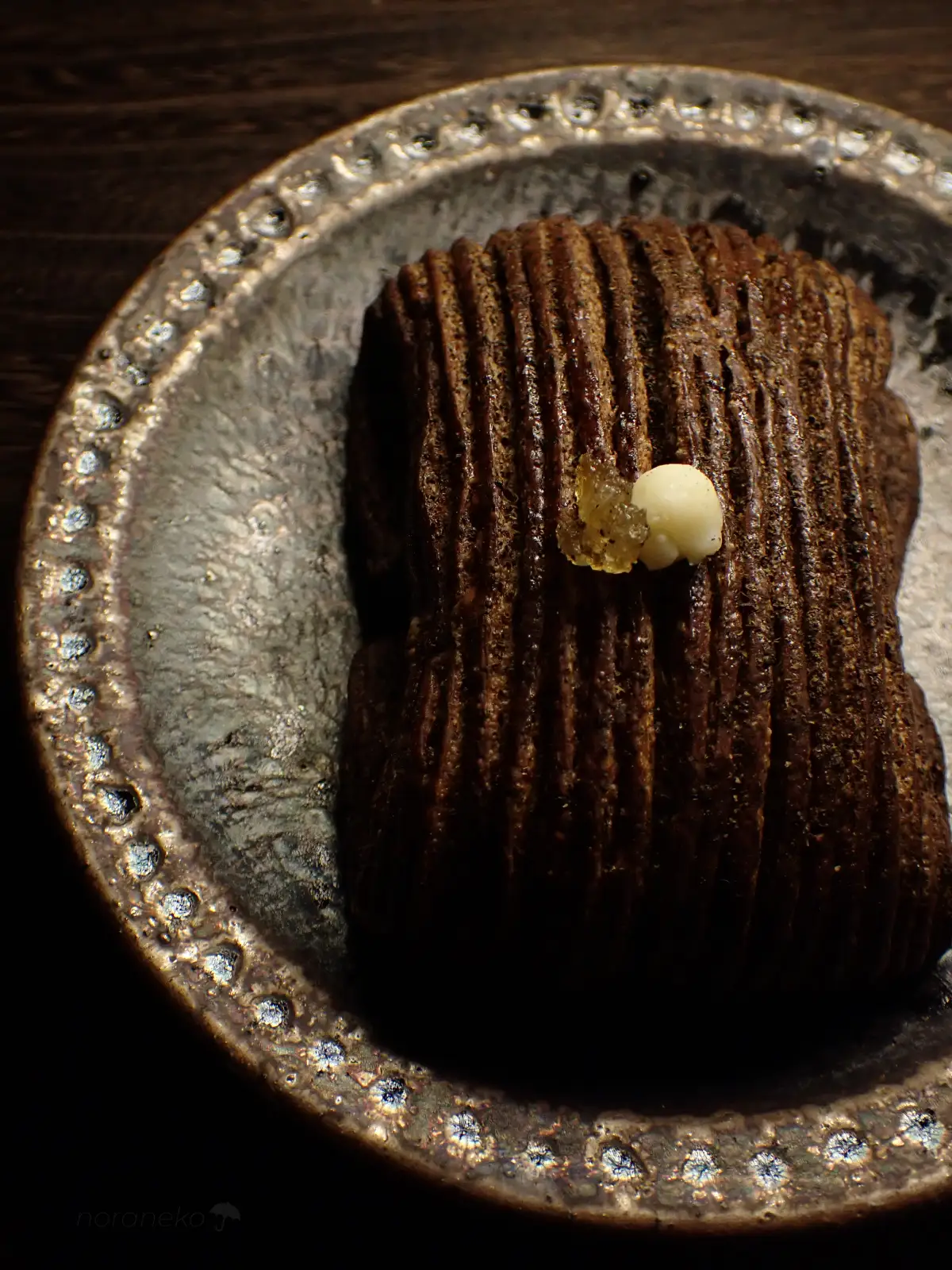 渋い金属のような光沢を持つ和皿にのせられた、bakery harry(ベーカリーハリー)の「パンスイス(ほうじ茶)」。ほうじ茶パウダーが練り込まれた深いブラウンのストライプ生地の質感。
