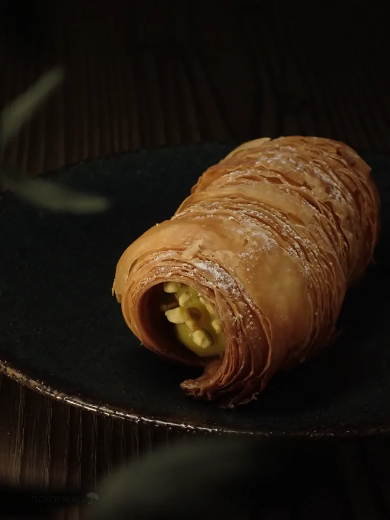 何層にも薄く重なったパリパリとした黄金色の生地の質感が美しい、LILAC BAKEの山鼻コロネピスタチオのアップ写真。